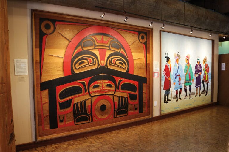 Large wooden carving with red and black design next to a painting of people