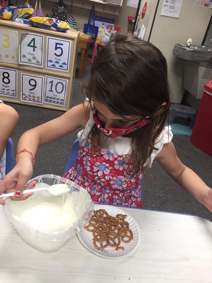 Child stirring white mixture in a bowl next to pretzels on a plate