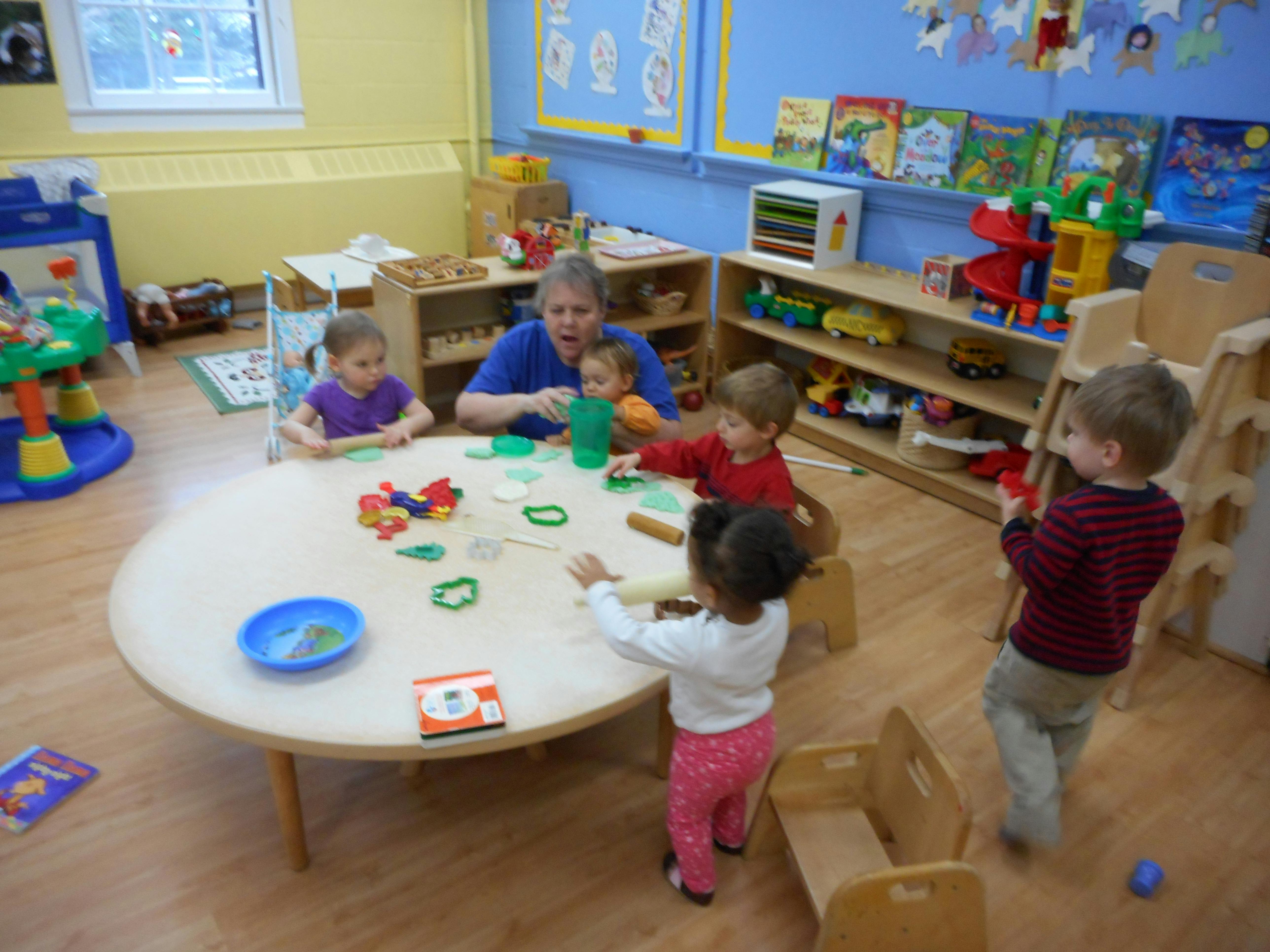 Adult and children playing with toys at a round table in a classroom