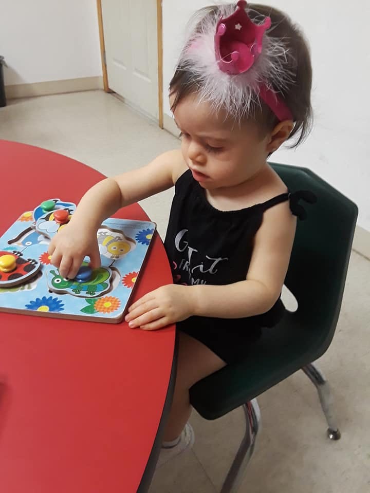 Child playing with a puzzle at a red table