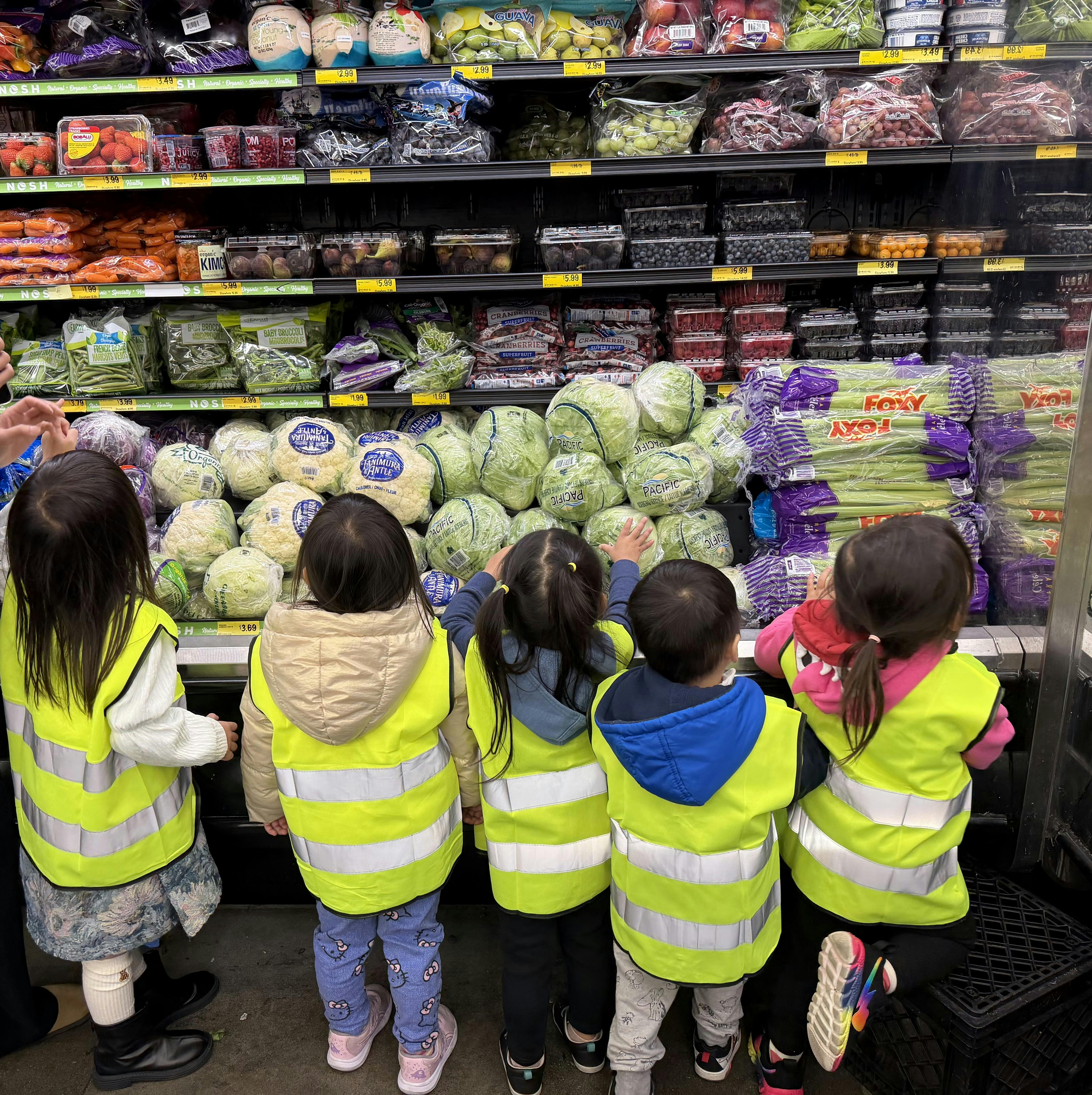 Group of children in bright yellow vests choosing vegetables at a grocery store