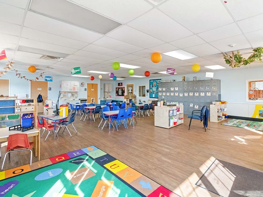 Classroom with small tables and chairs, cubbies, and a colorful alphabet rug