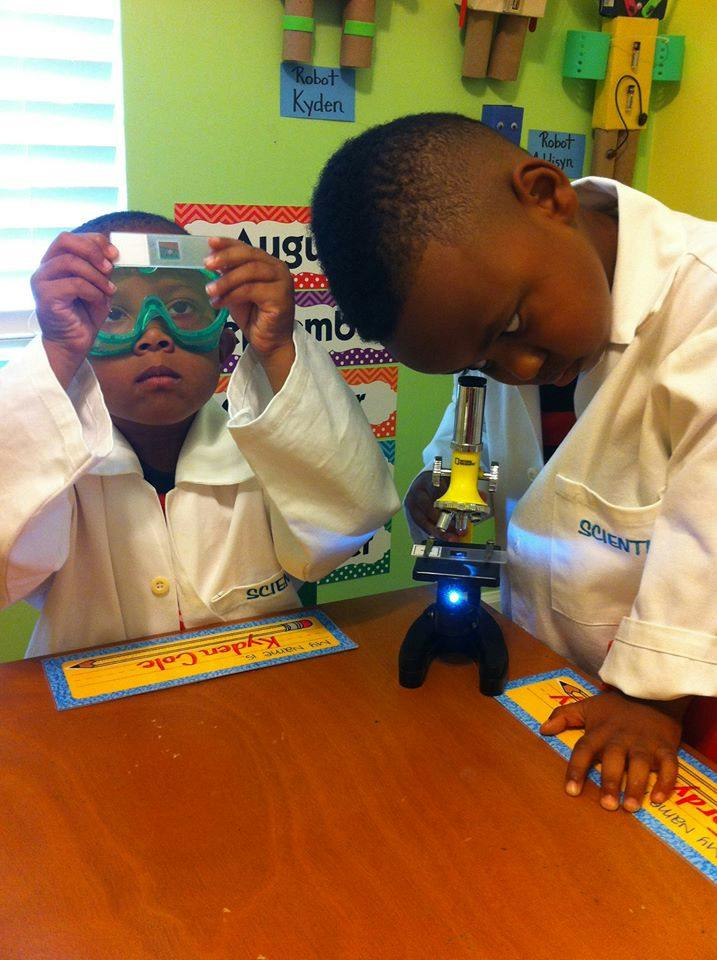 Two children in lab coats using a microscope and holding a slide