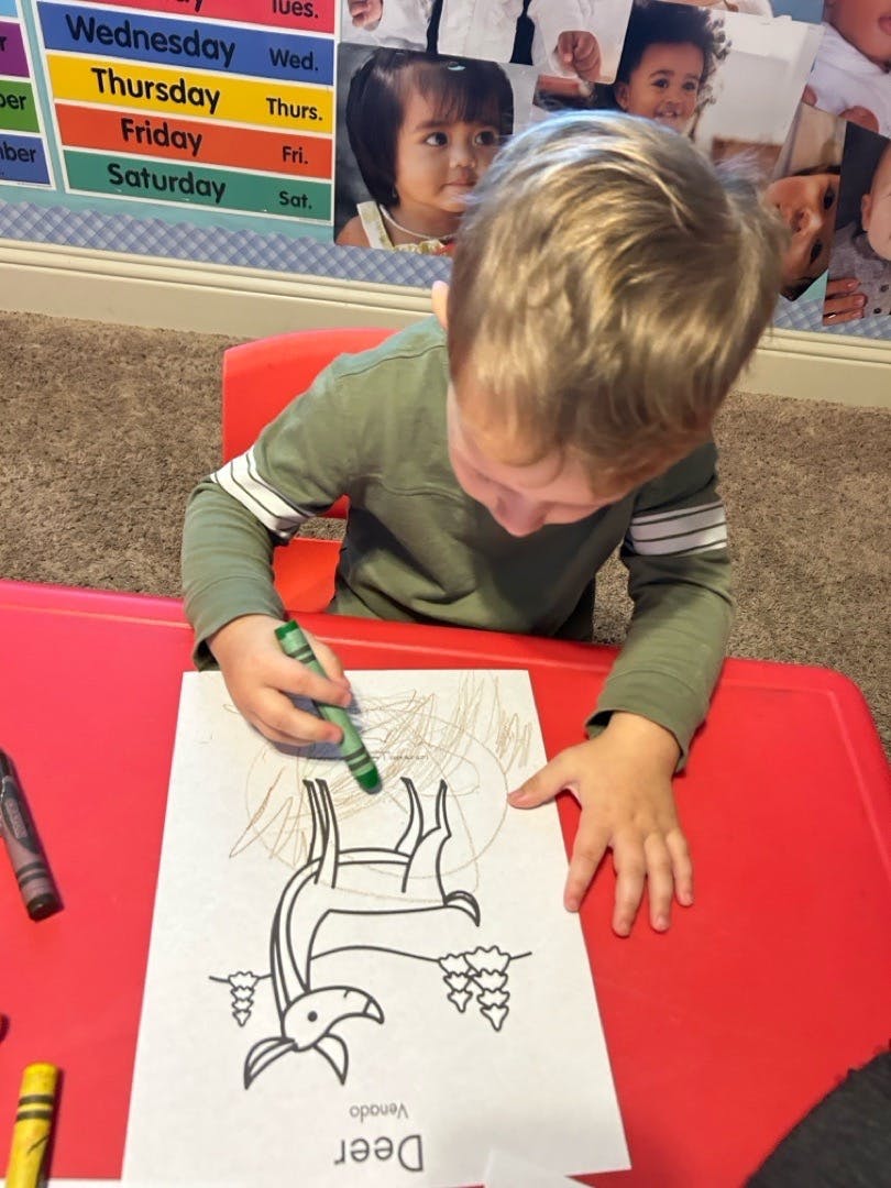 Child coloring a deer drawing with a green crayon