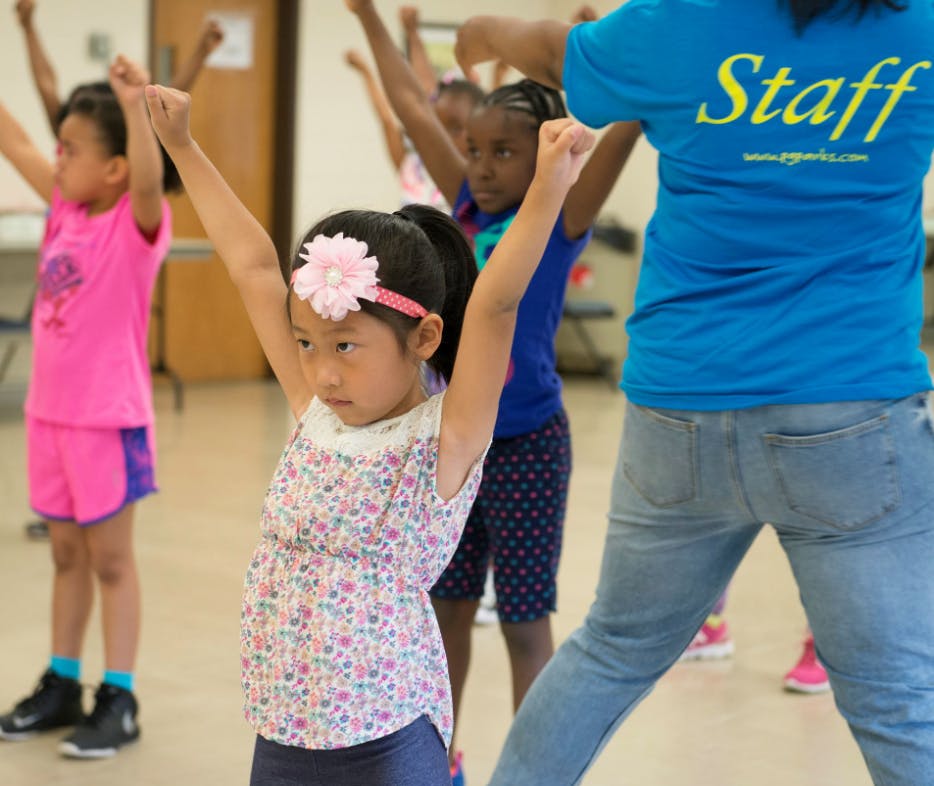 Children and an adult with arms raised in a classroom