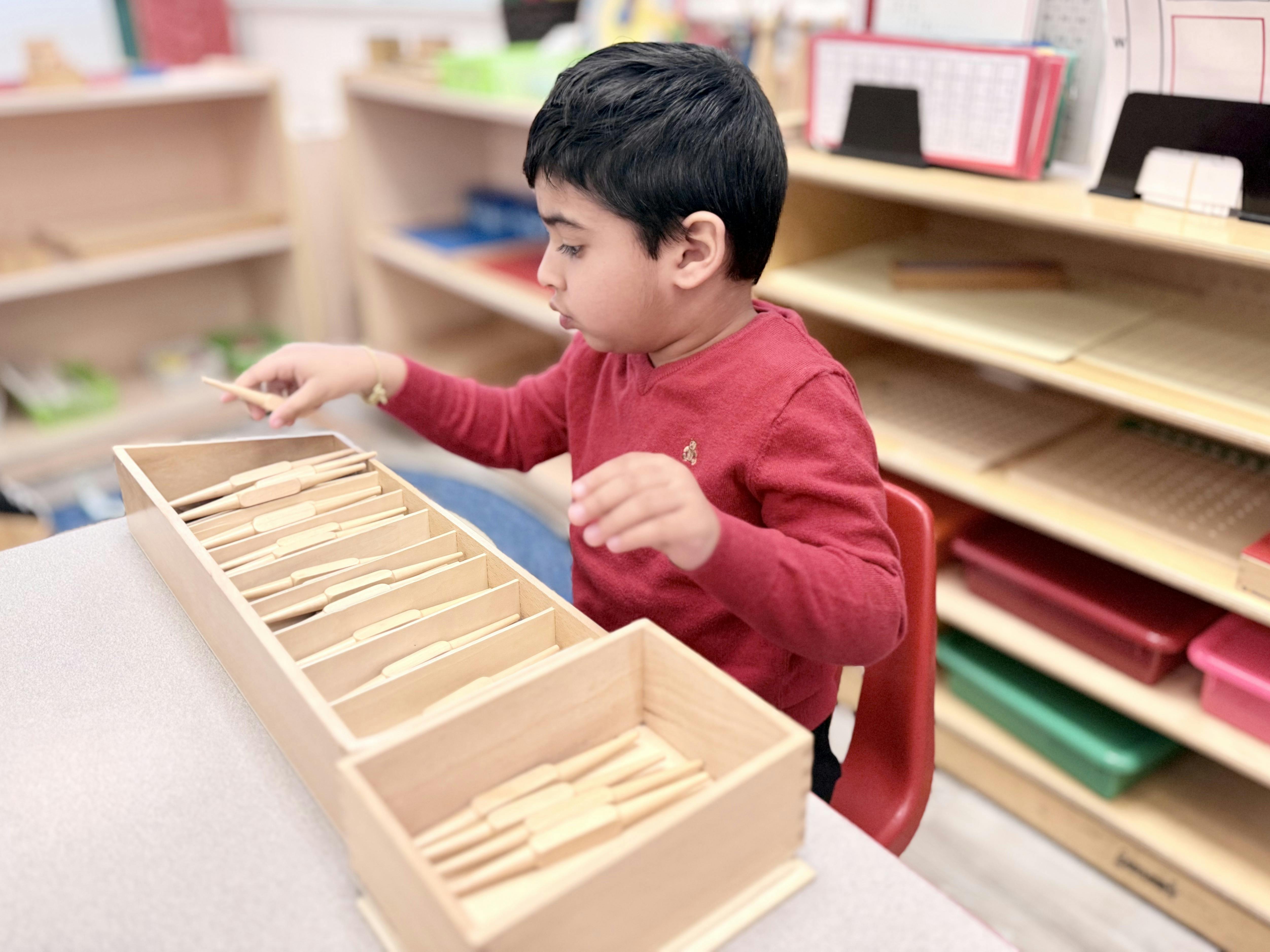 Child in a classroom selecting wooden blocks from a partitioned box