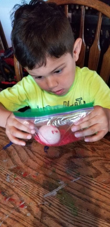 Child holding a plastic bag with a white egg and red material inside