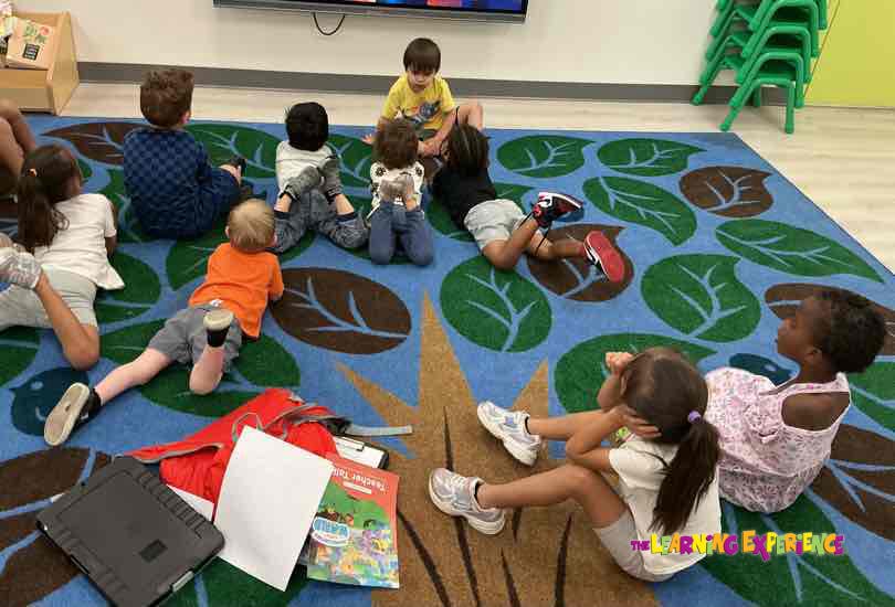 Children sitting on a rug with a leaf pattern, facing forward