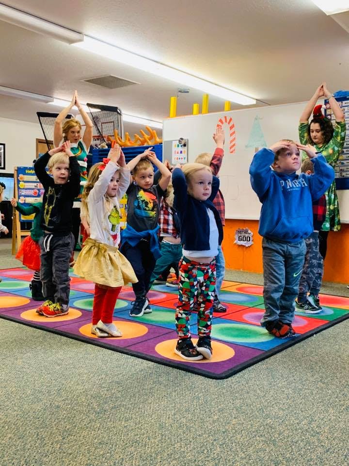 Adults and children standing on a colorful mat with hands raised