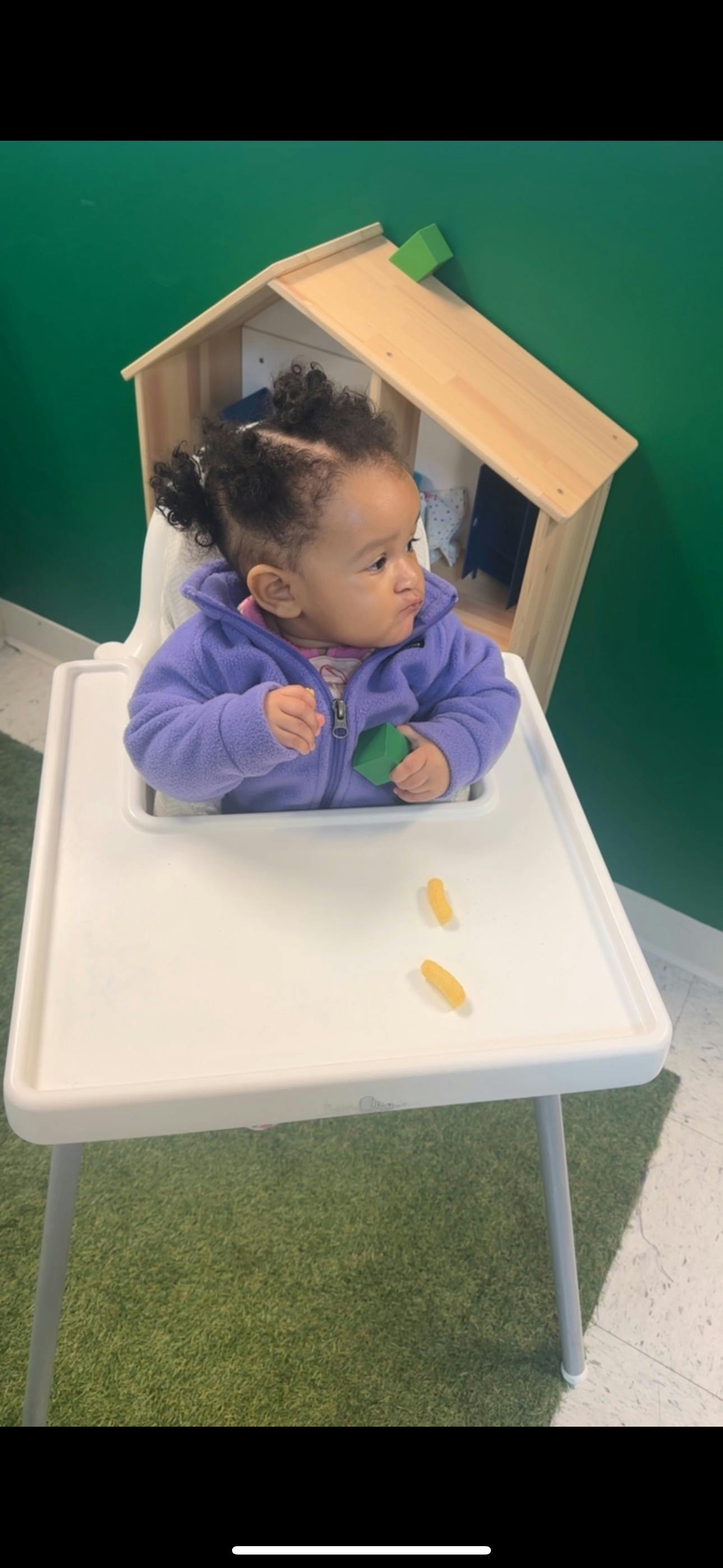 Child in a high chair holding a green block