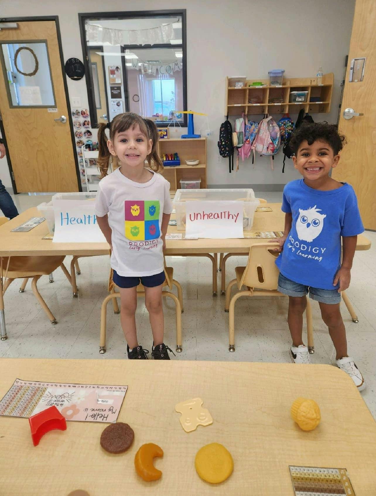 Two children standing behind tables with "Healthy" and "Unhealthy" signs