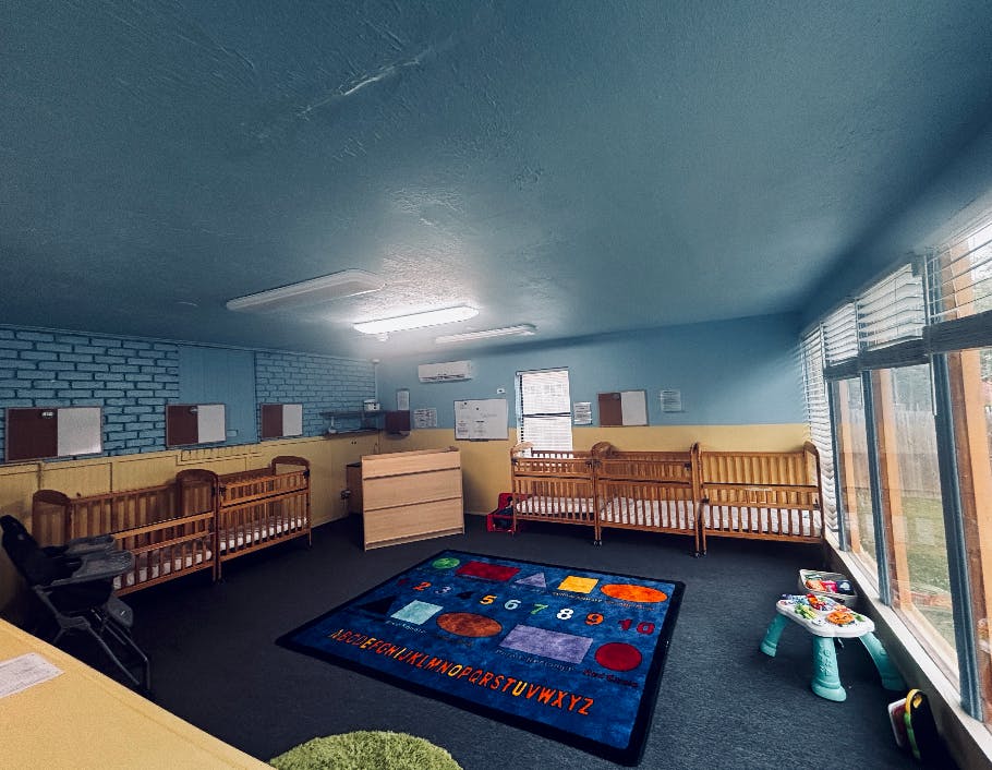 Cribs and a colorful educational rug in a daycare room