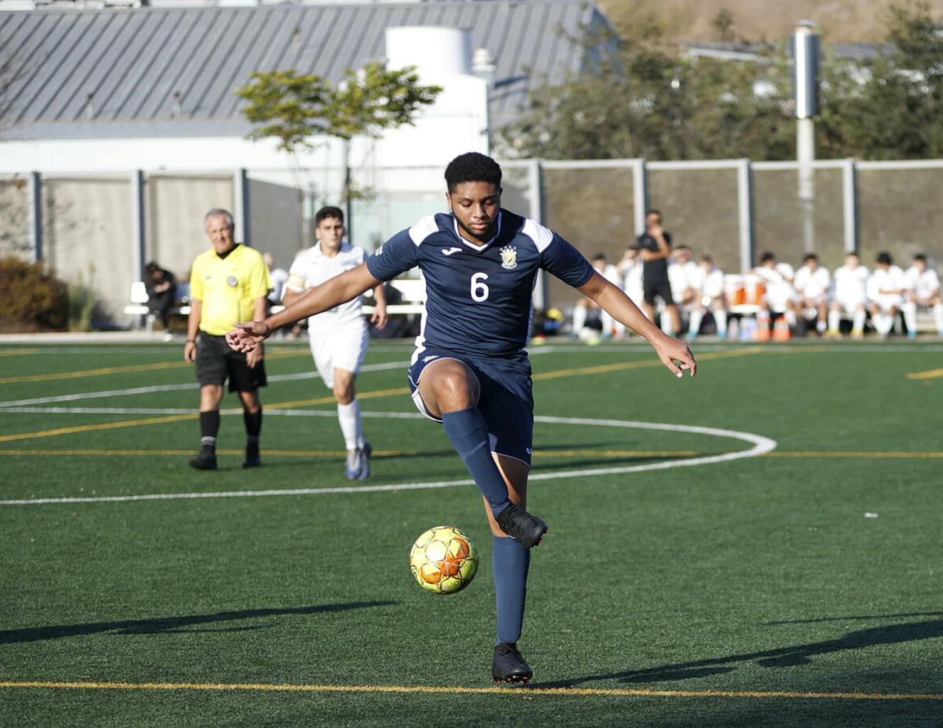 Person in a blue uniform kicking a soccer ball on a field