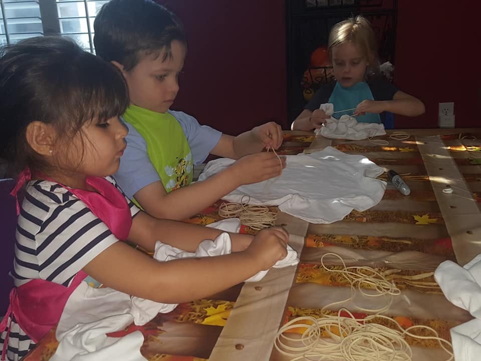 Three children tie-dyeing fabric at a table
