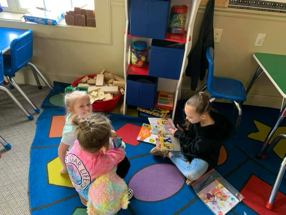 Three children playing on a rug in a classroom