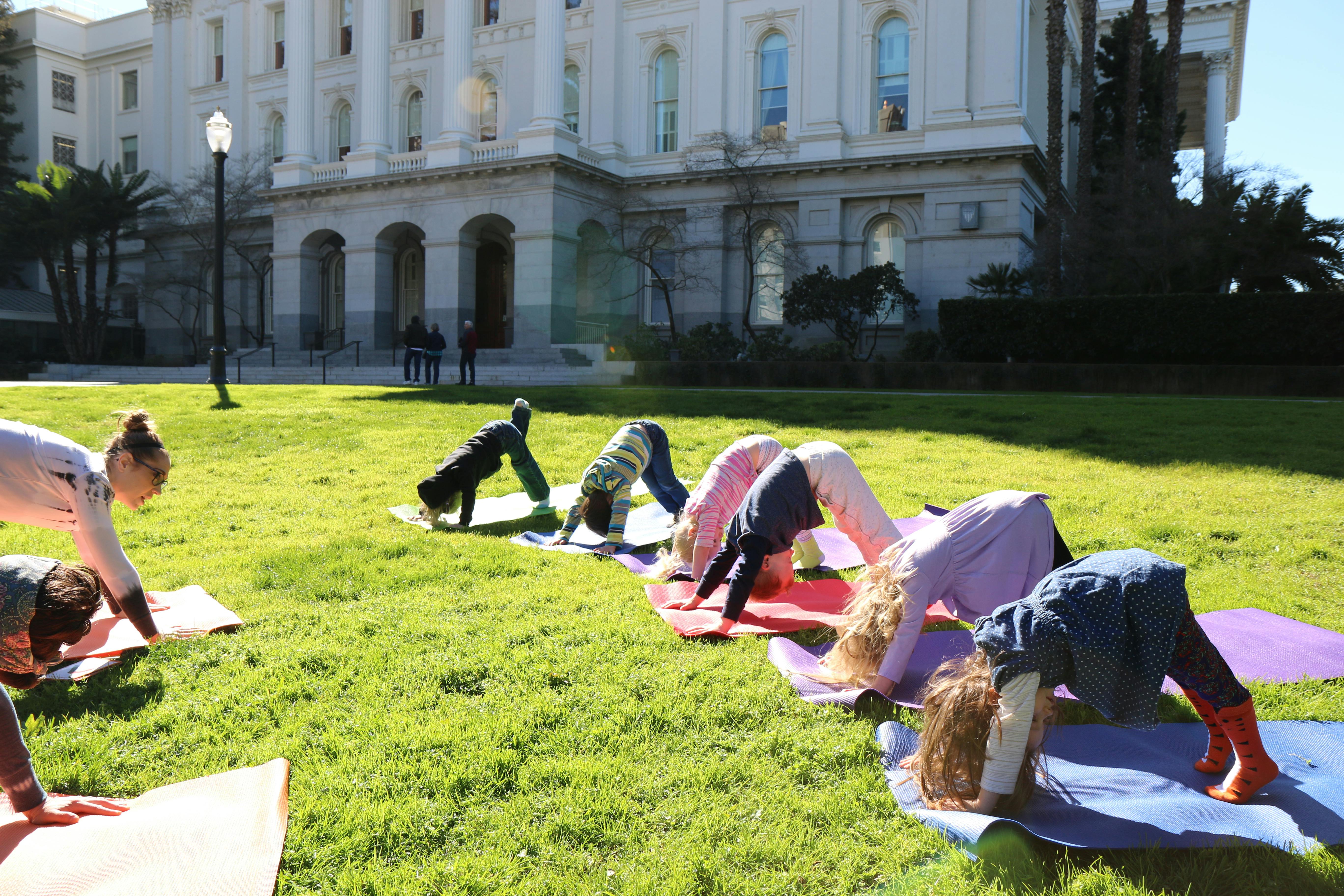 Group of children and an adult practicing yoga on mats in a park