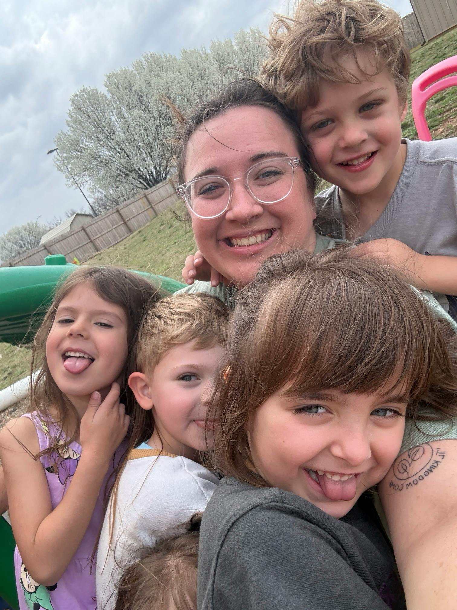 Smiling person in glasses with four children sticking out their tongues