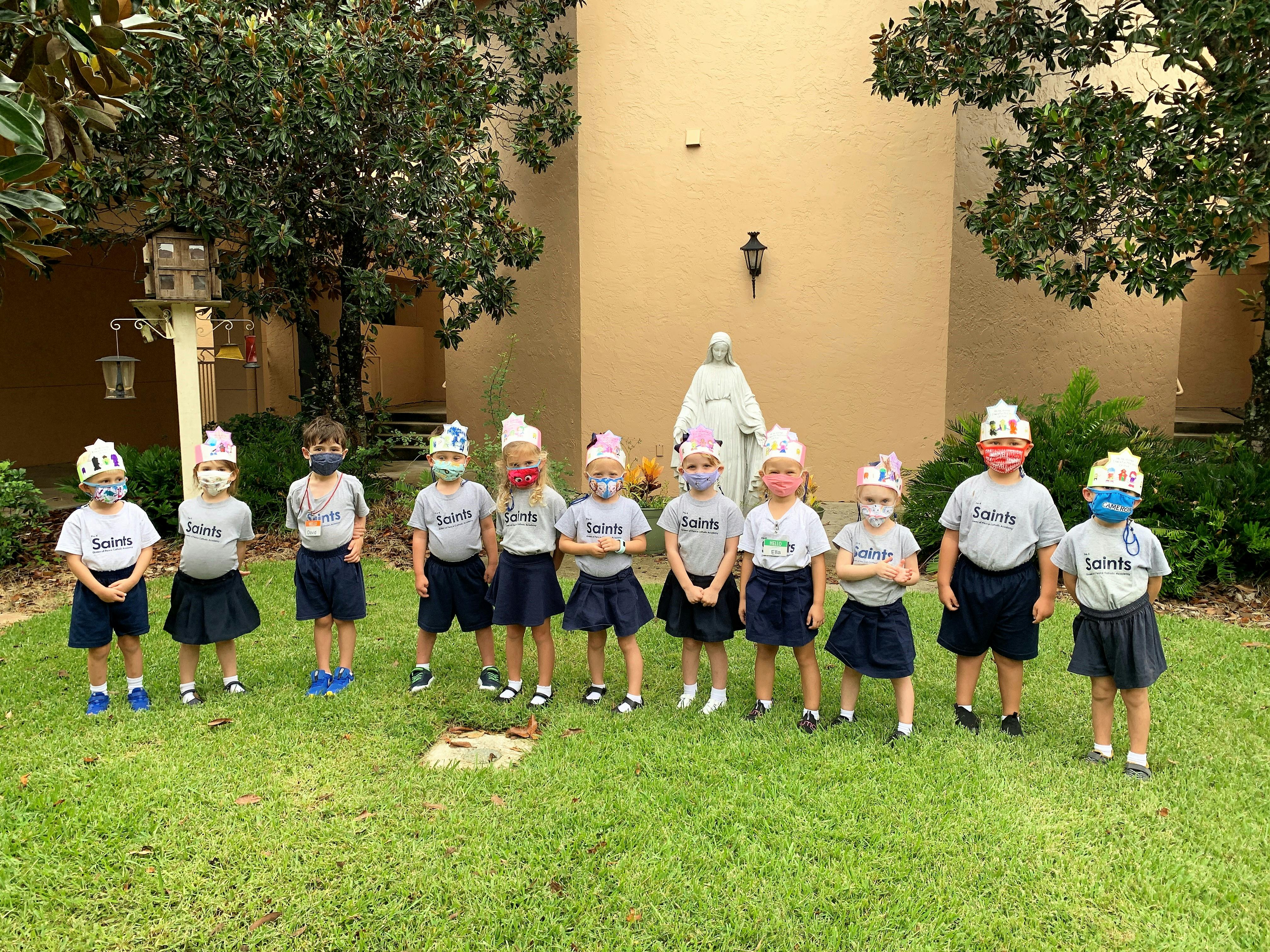 Group of children wearing masks and paper crowns standing on grass