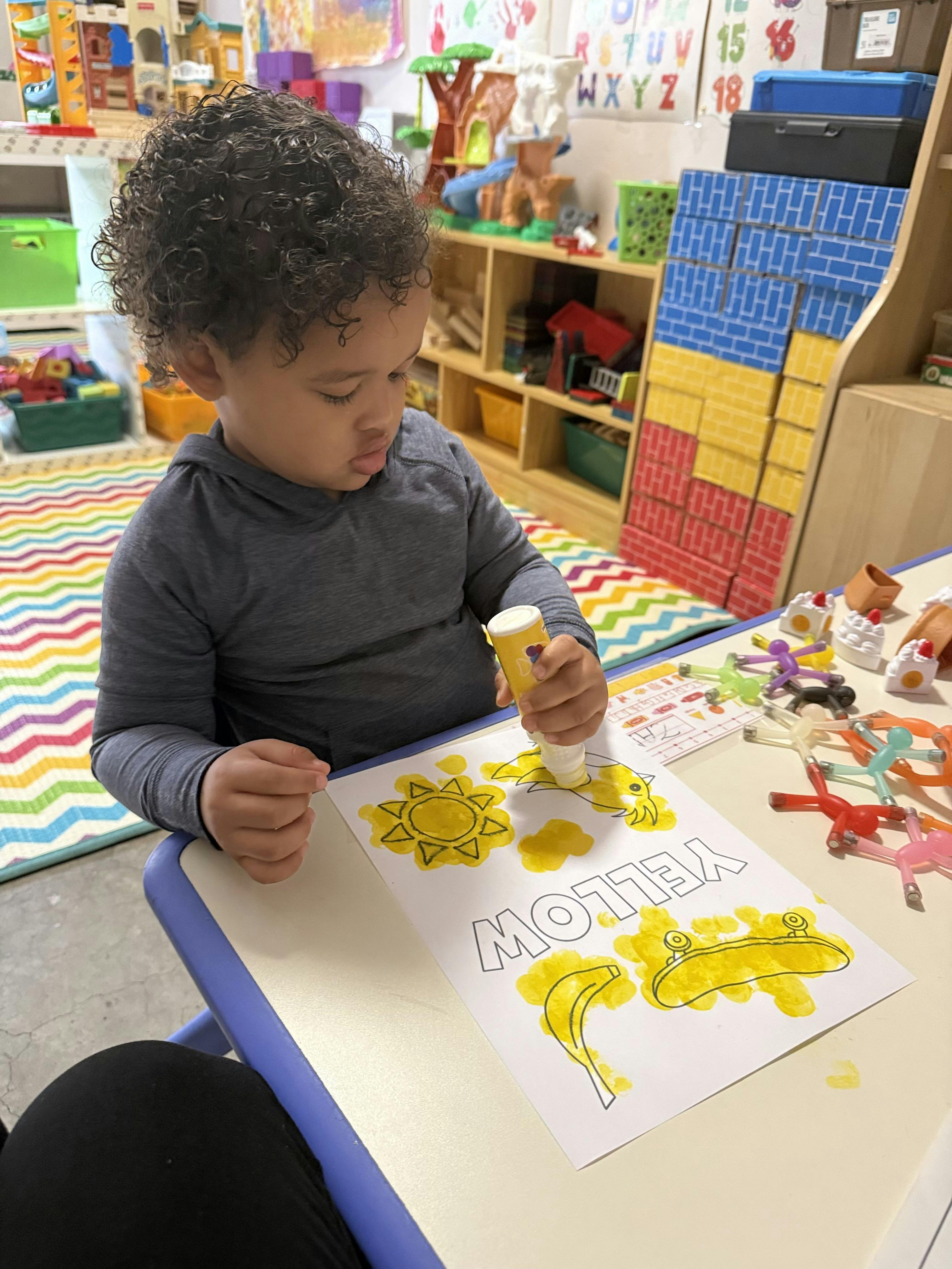 Child using a yellow dot marker on a worksheet in a classroom