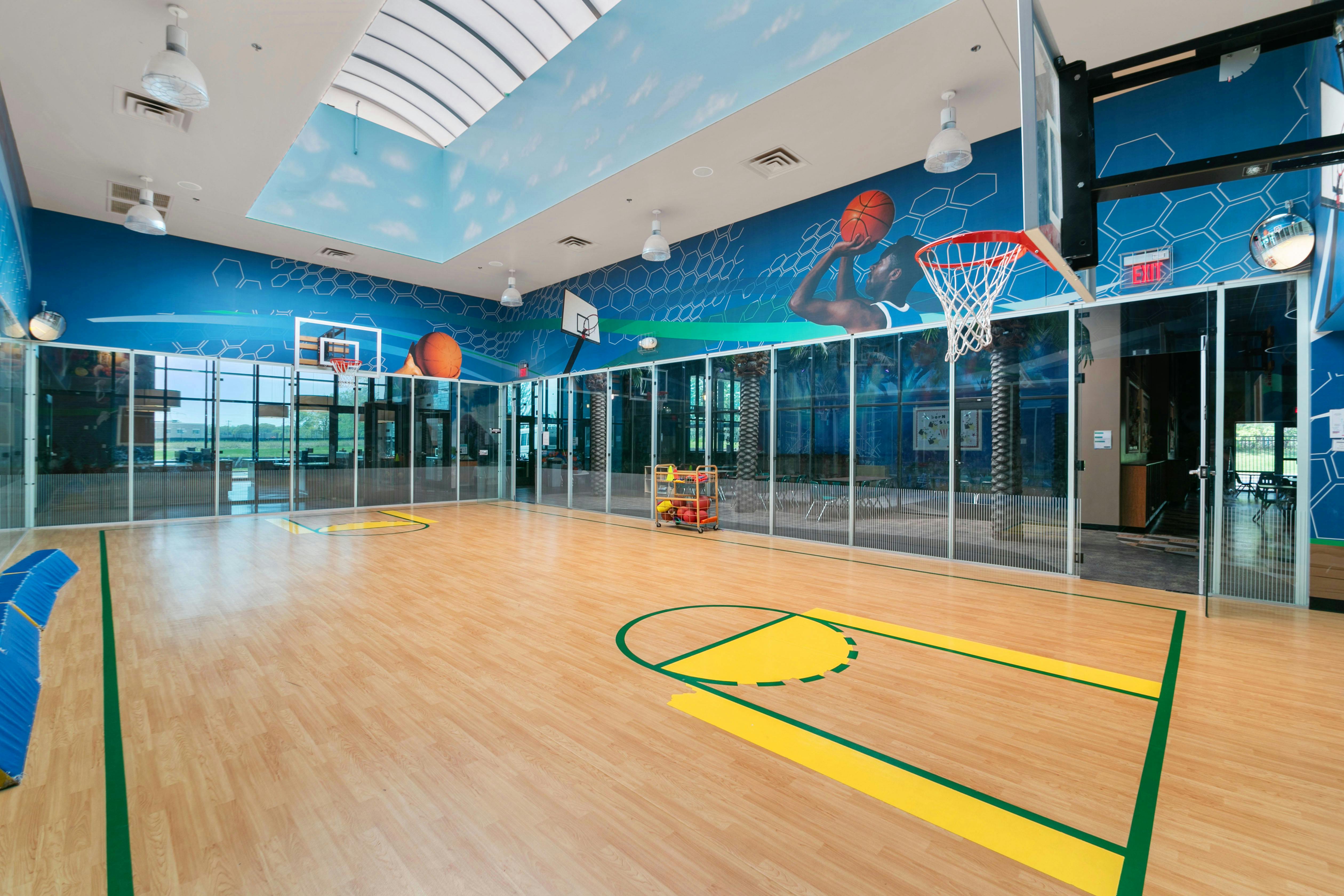Indoor basketball court with two hoops, light wood floor, and blue and white walls