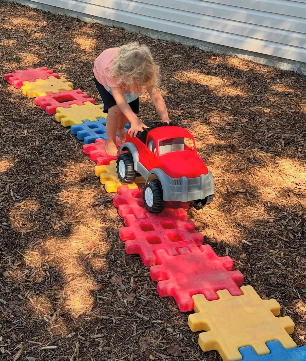 Child pushing a toy truck on a path of colorful interlocking mats
