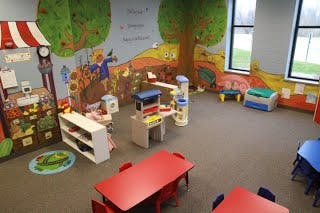 Playroom with colorful wall murals, small tables, and play structures