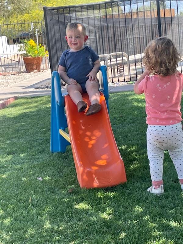 Child sitting on a slide with another child standing nearby