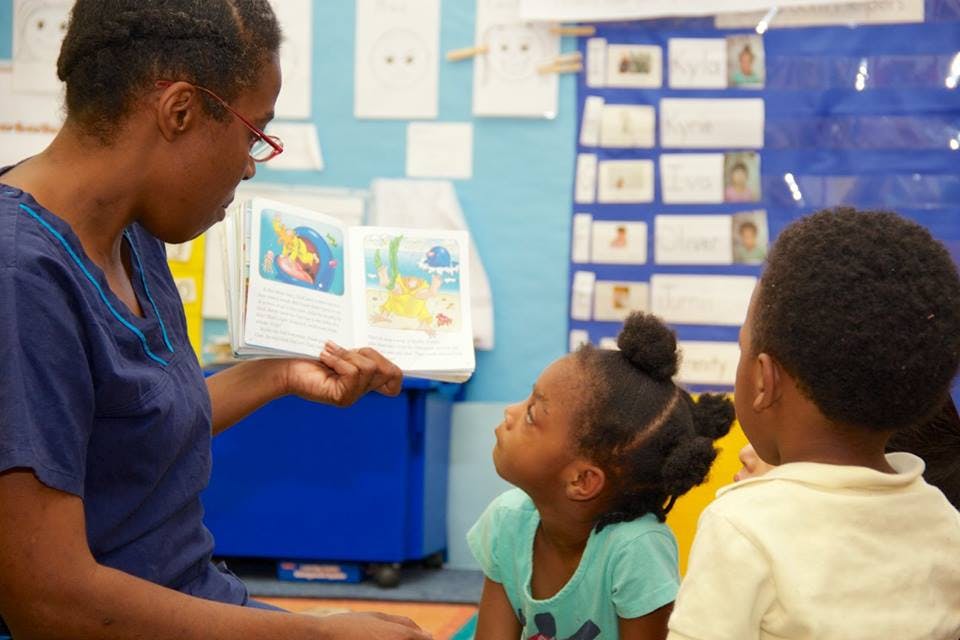 Person reading a book to two children in a classroom
