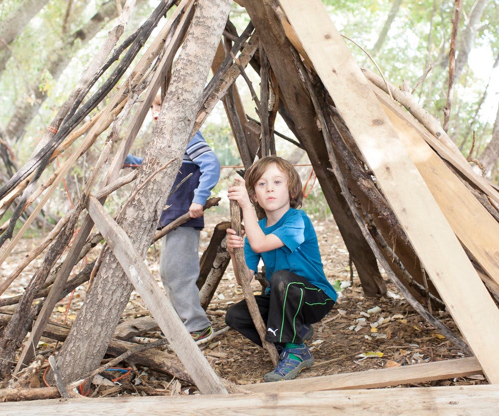 Child crouching inside a stick fort
