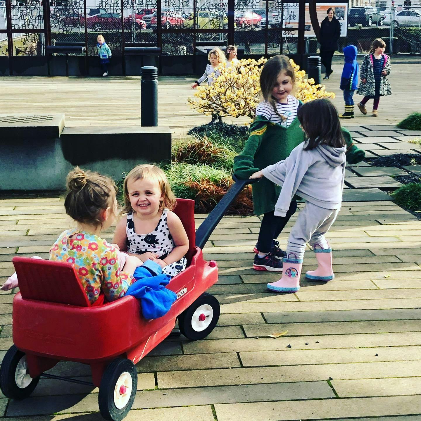 Two children in a red wagon, another child pulling the wagon