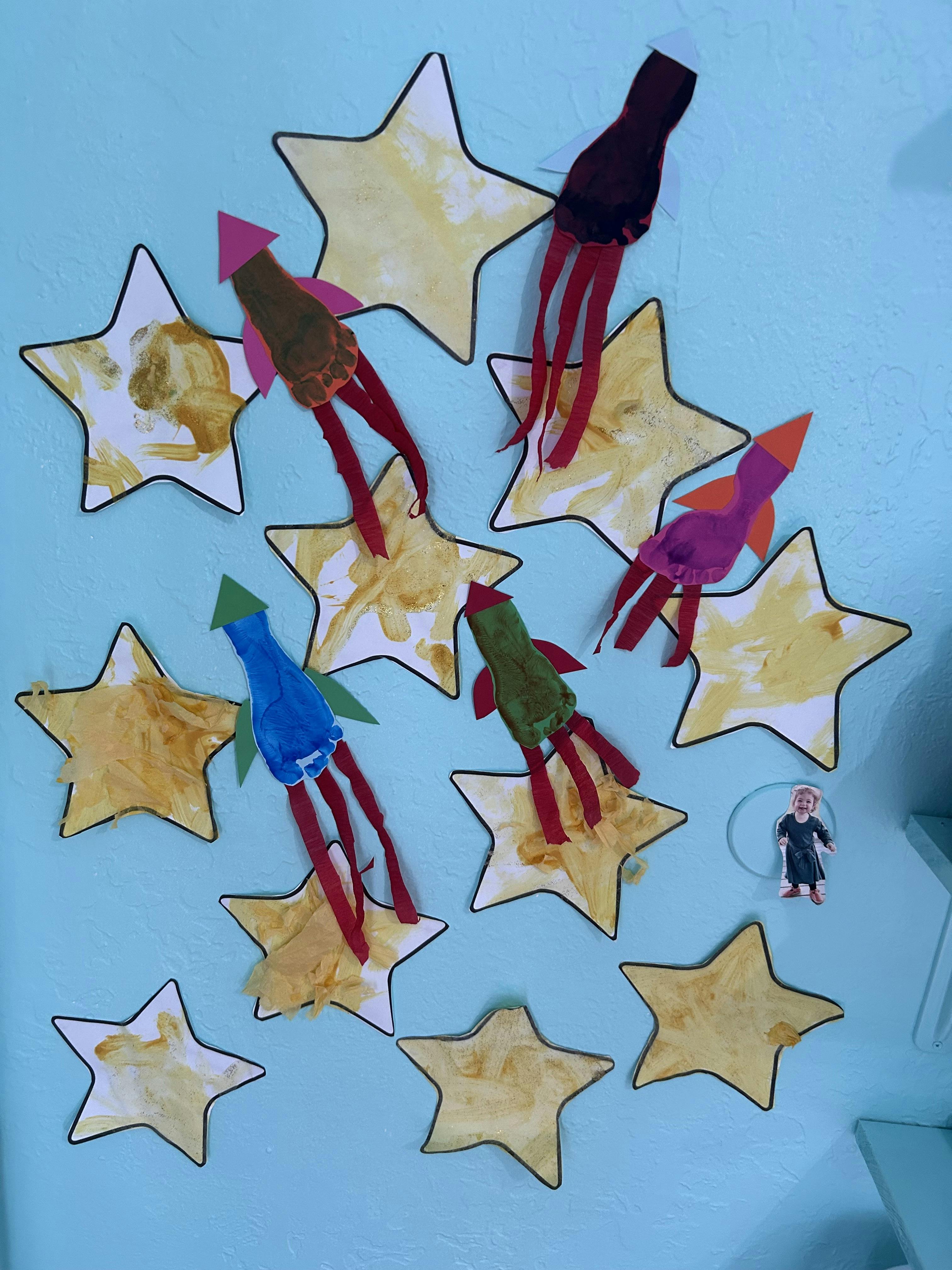 Paper stars and footprint rocket ship crafts displayed on a light blue wall