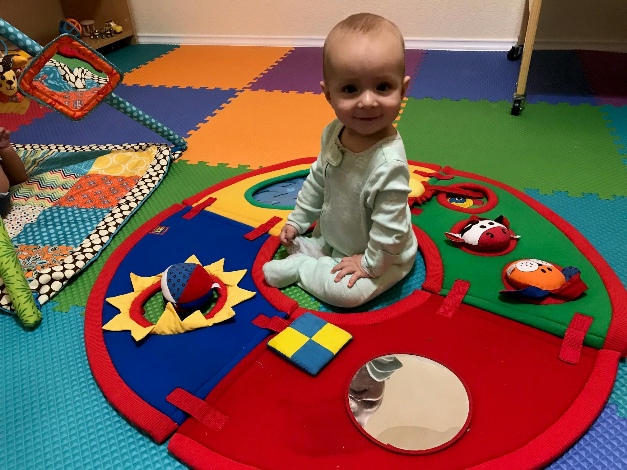 Child sitting on a colorful playmat with toys