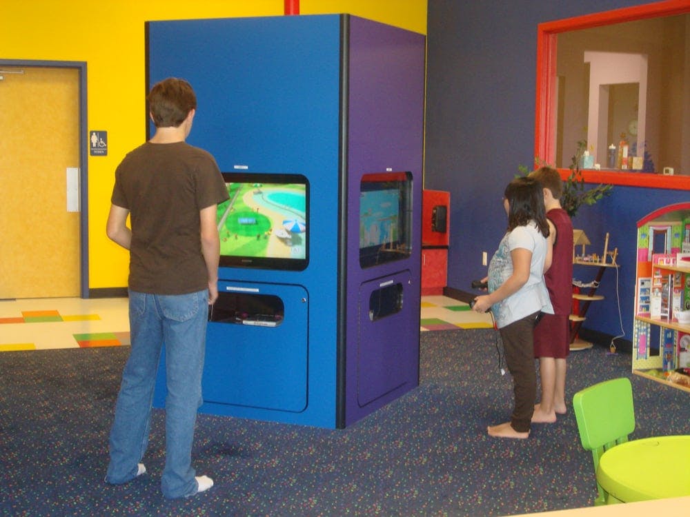 Person playing a video game on a blue console, two people watching another screen