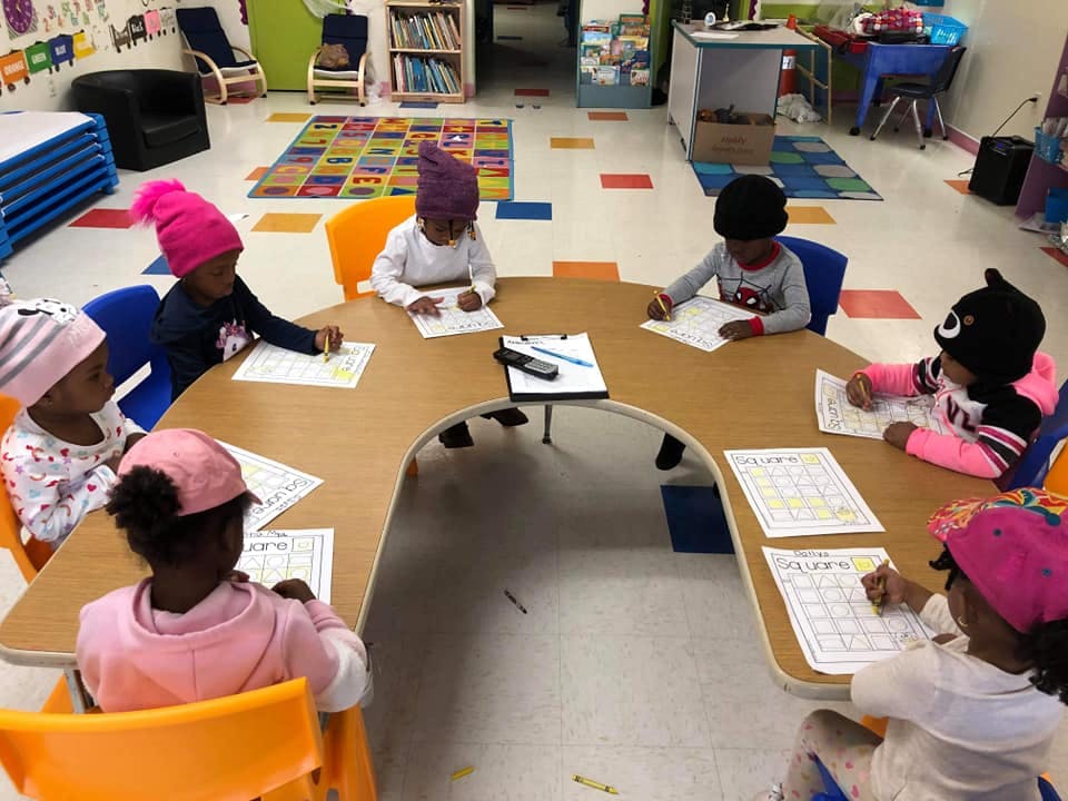 Children sitting at a table in a classroom, writing on papers