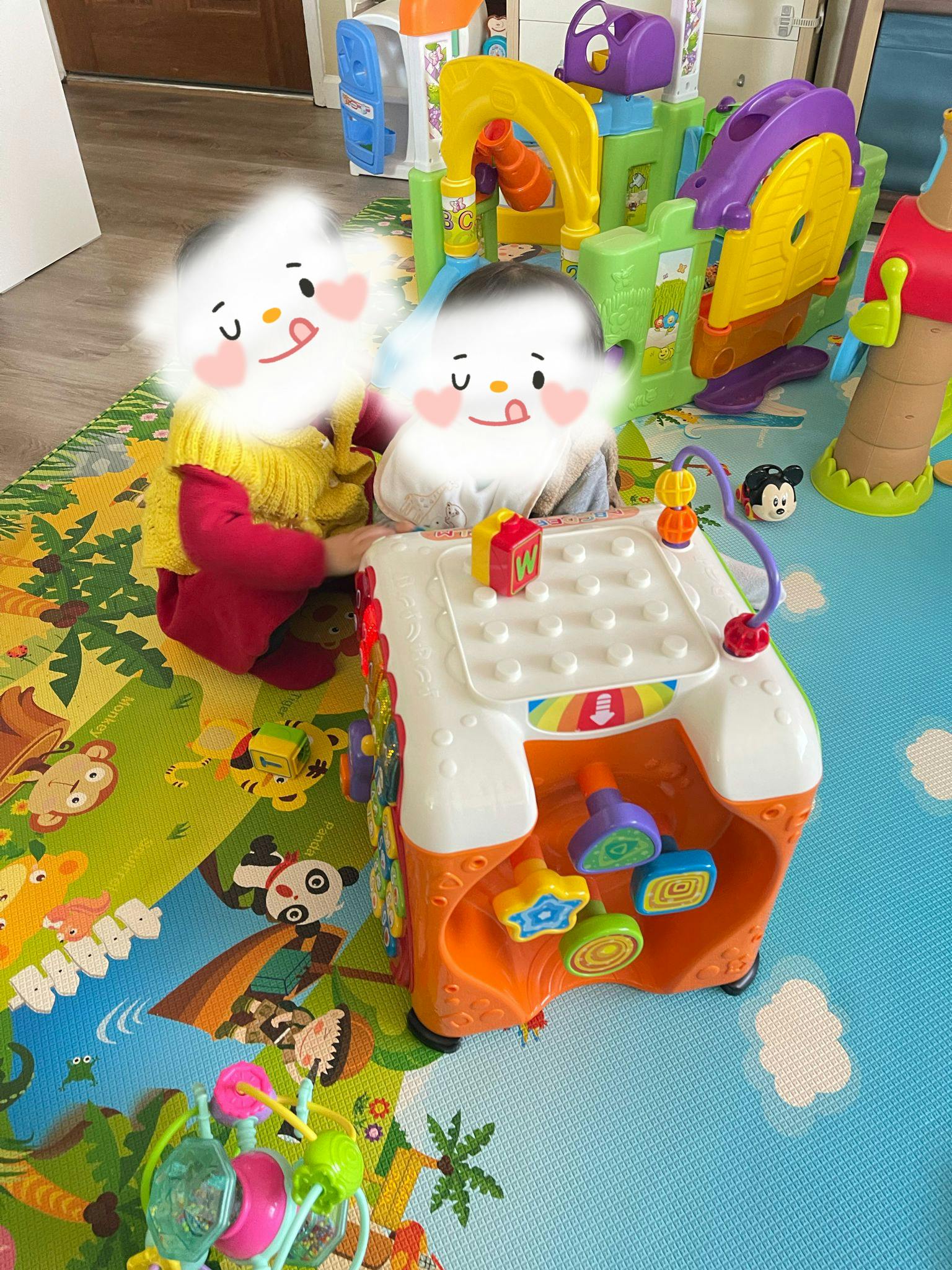 Two children playing with a colorful activity table on a patterned mat