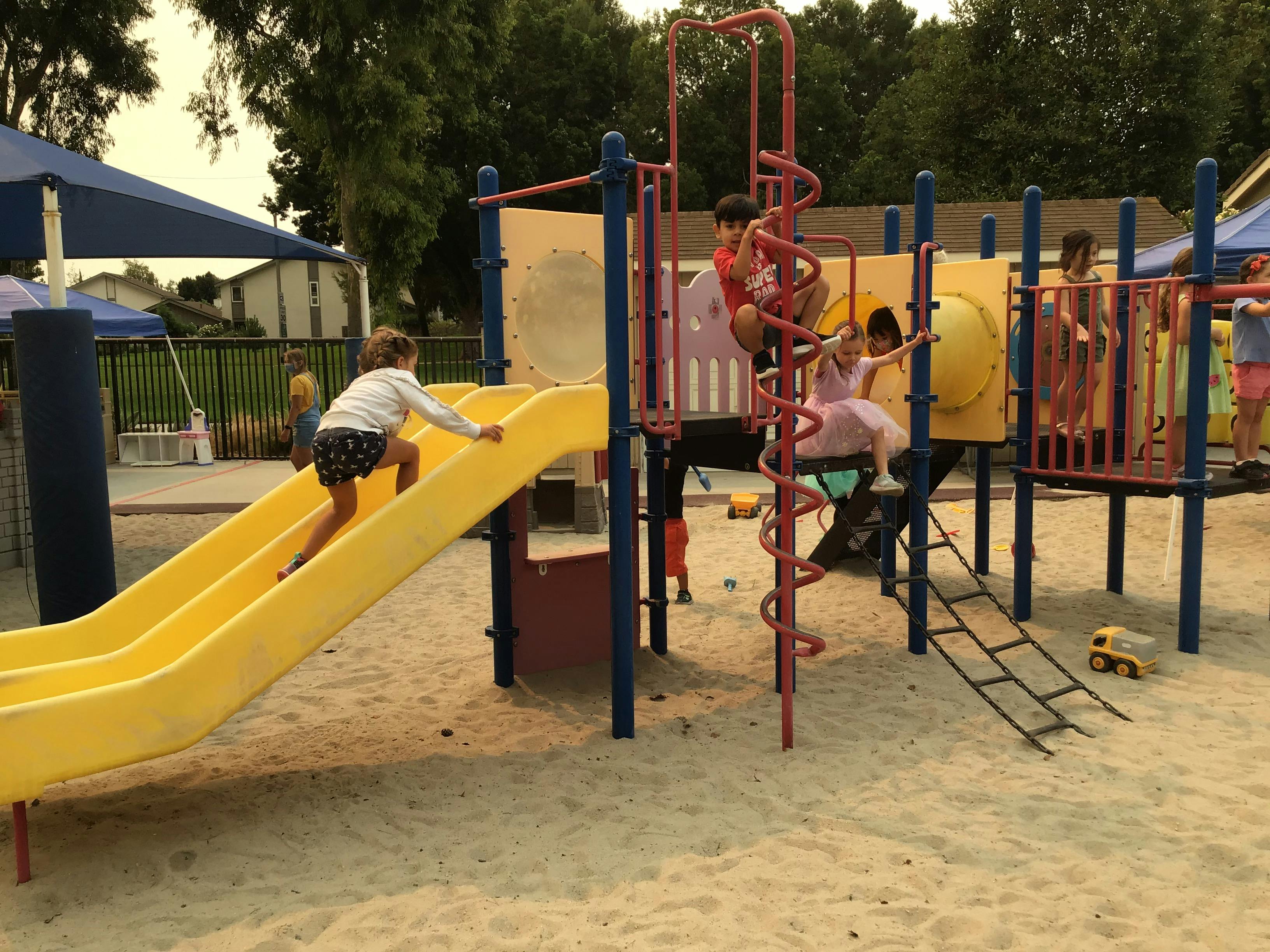 Children playing on a playground structure with slides and climbing structures