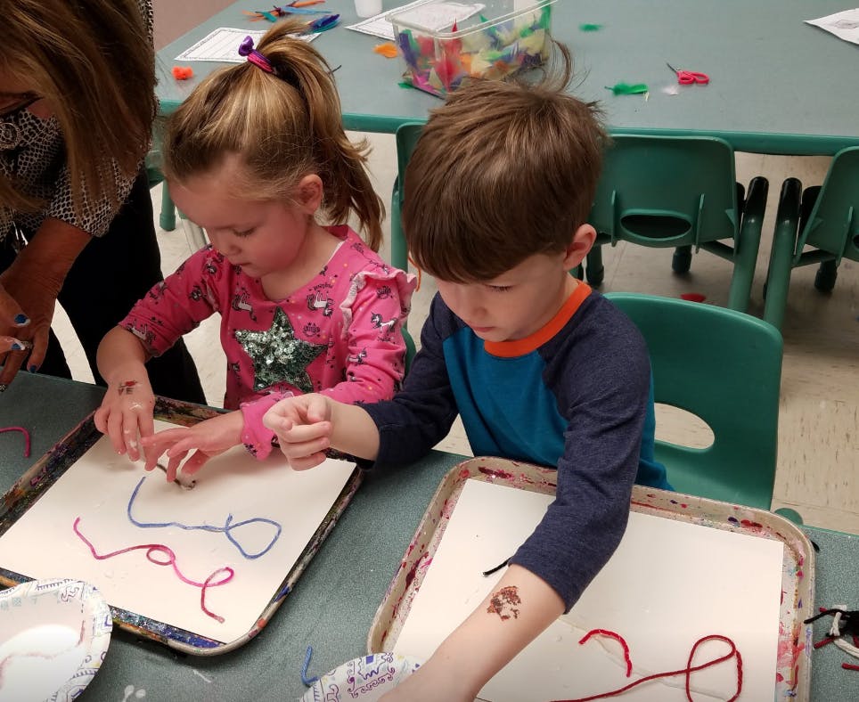 Two children doing an art activity with yarn on trays