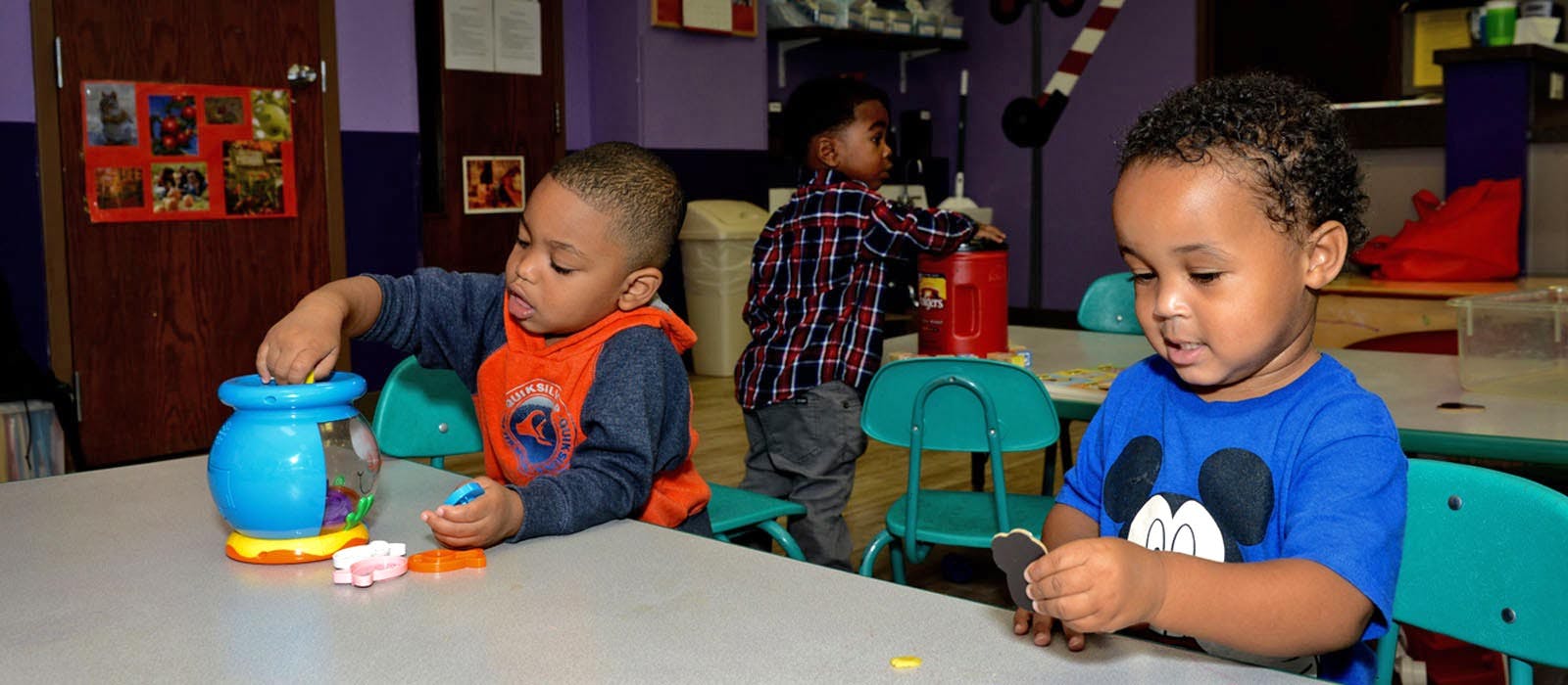 Three children playing with toys at a table in a classroom