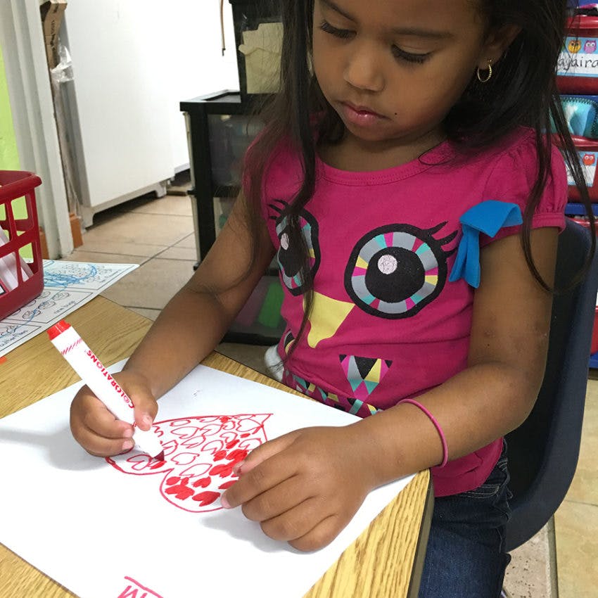 Child drawing a heart on paper with a red marker