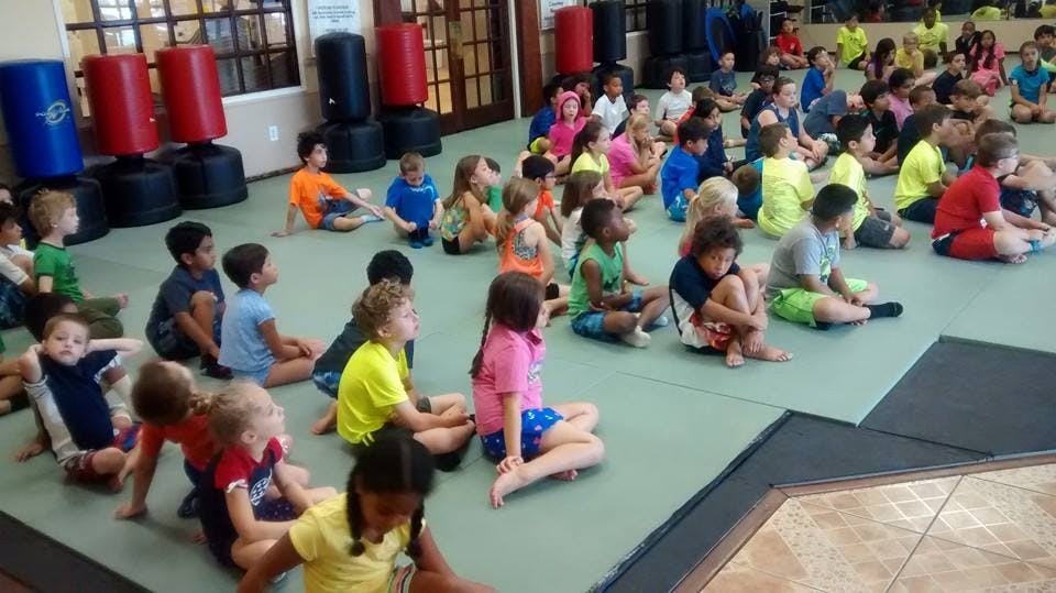 Many children sitting on a mat in a large room