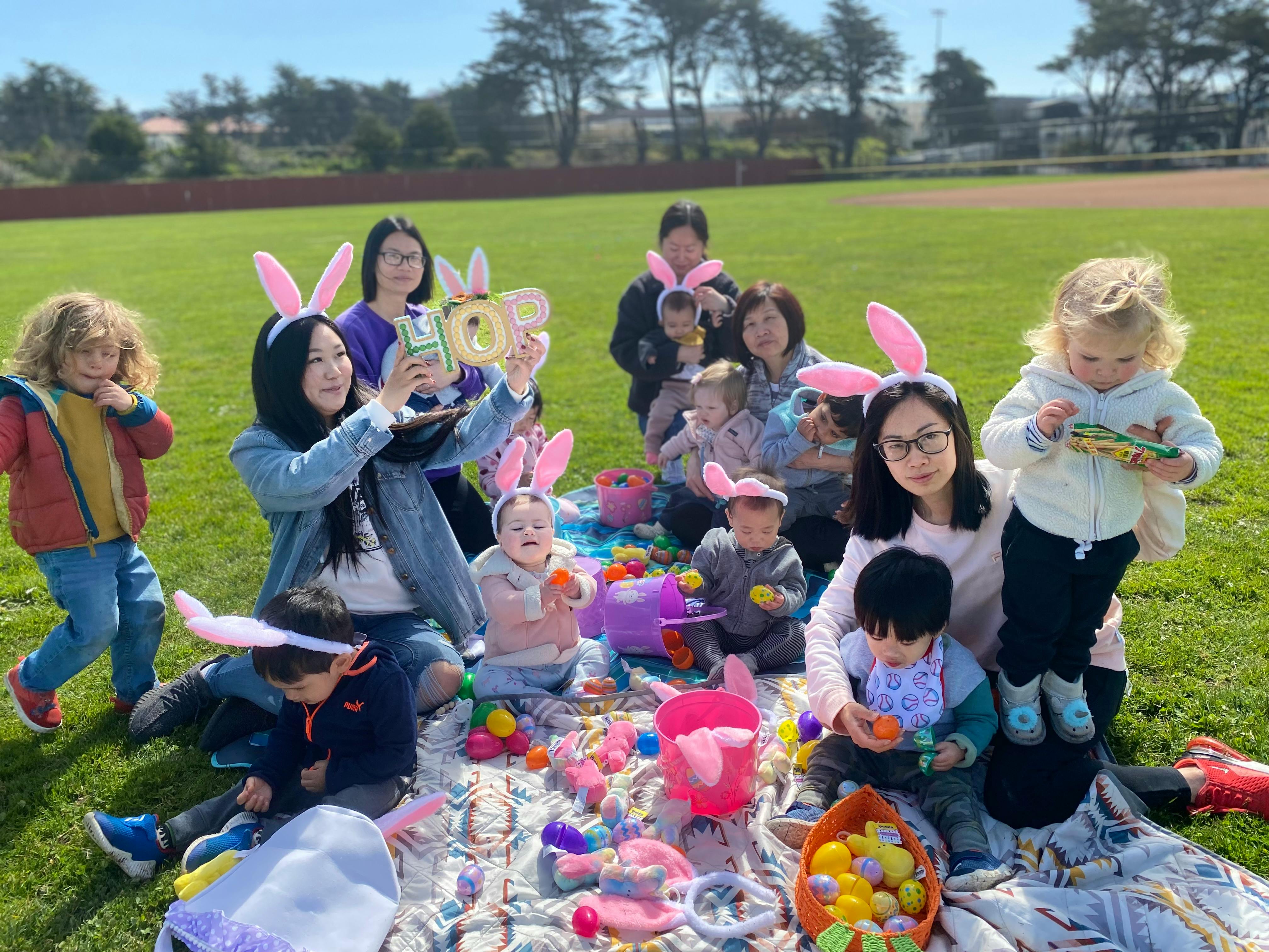 People and children wearing bunny ears at an outdoor Easter egg hunt