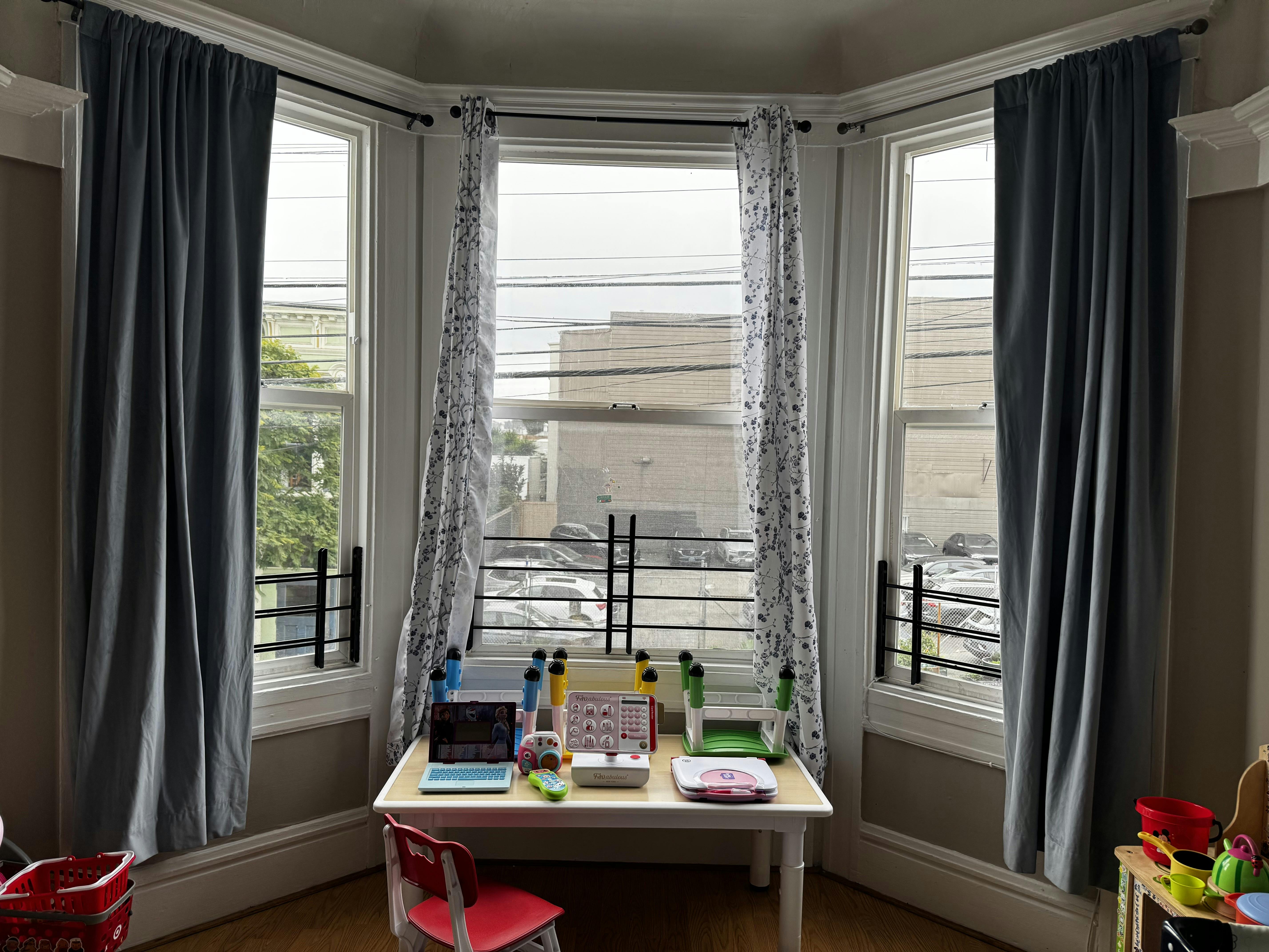 Children's table with a toy laptop and other play items in a bay window