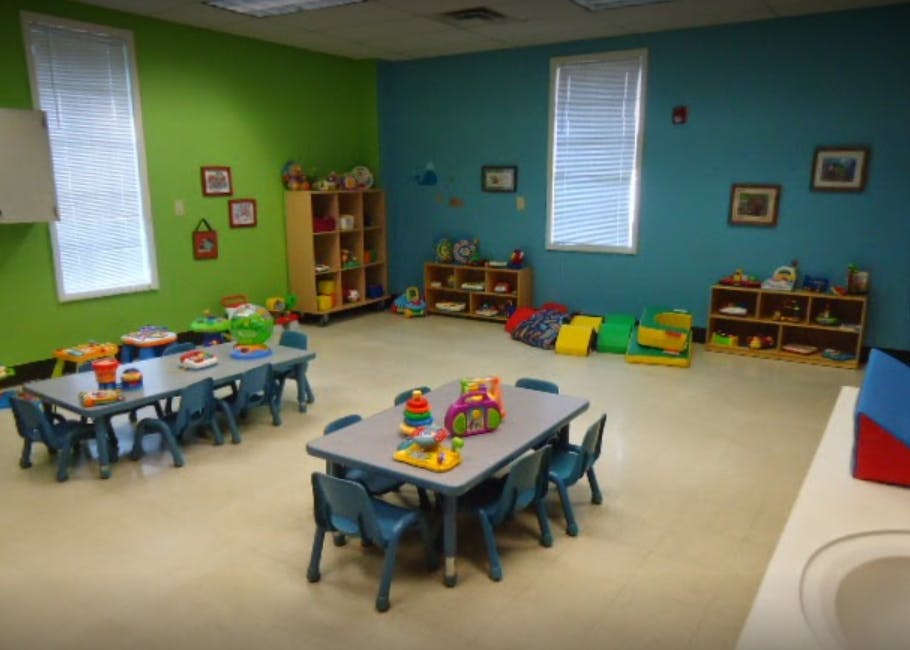 Classroom with small tables and chairs, shelves with toys