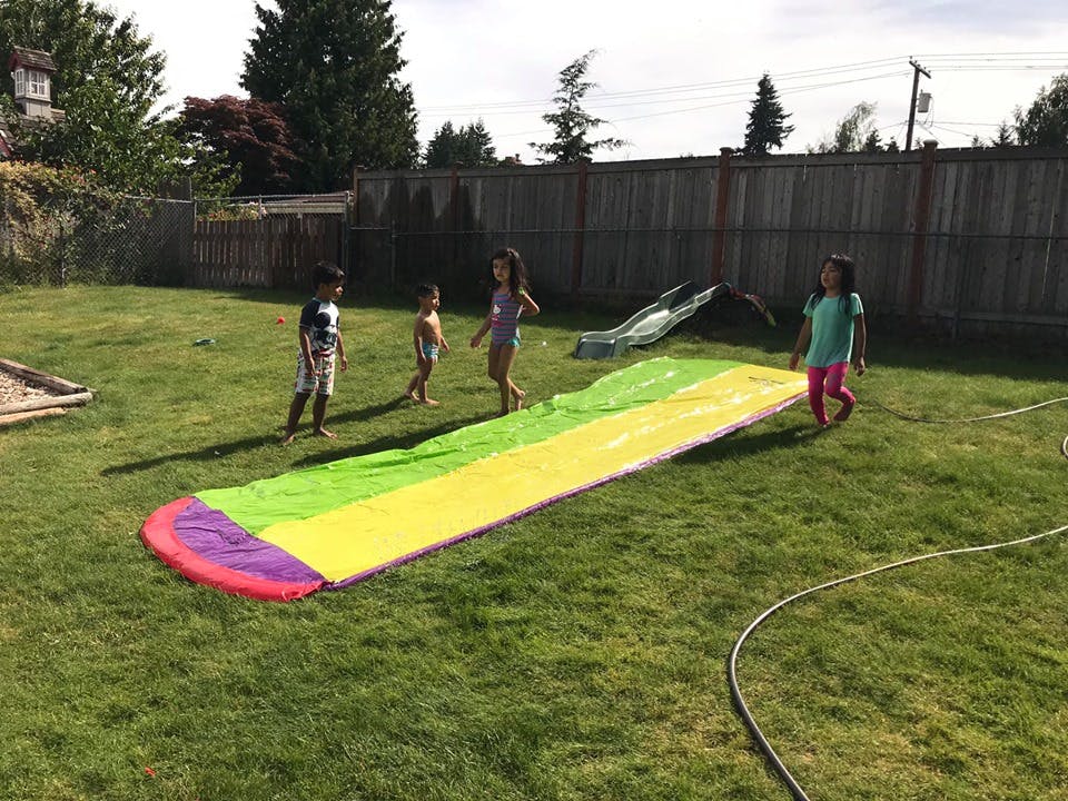 Children playing on a slip and slide in a grassy backyard