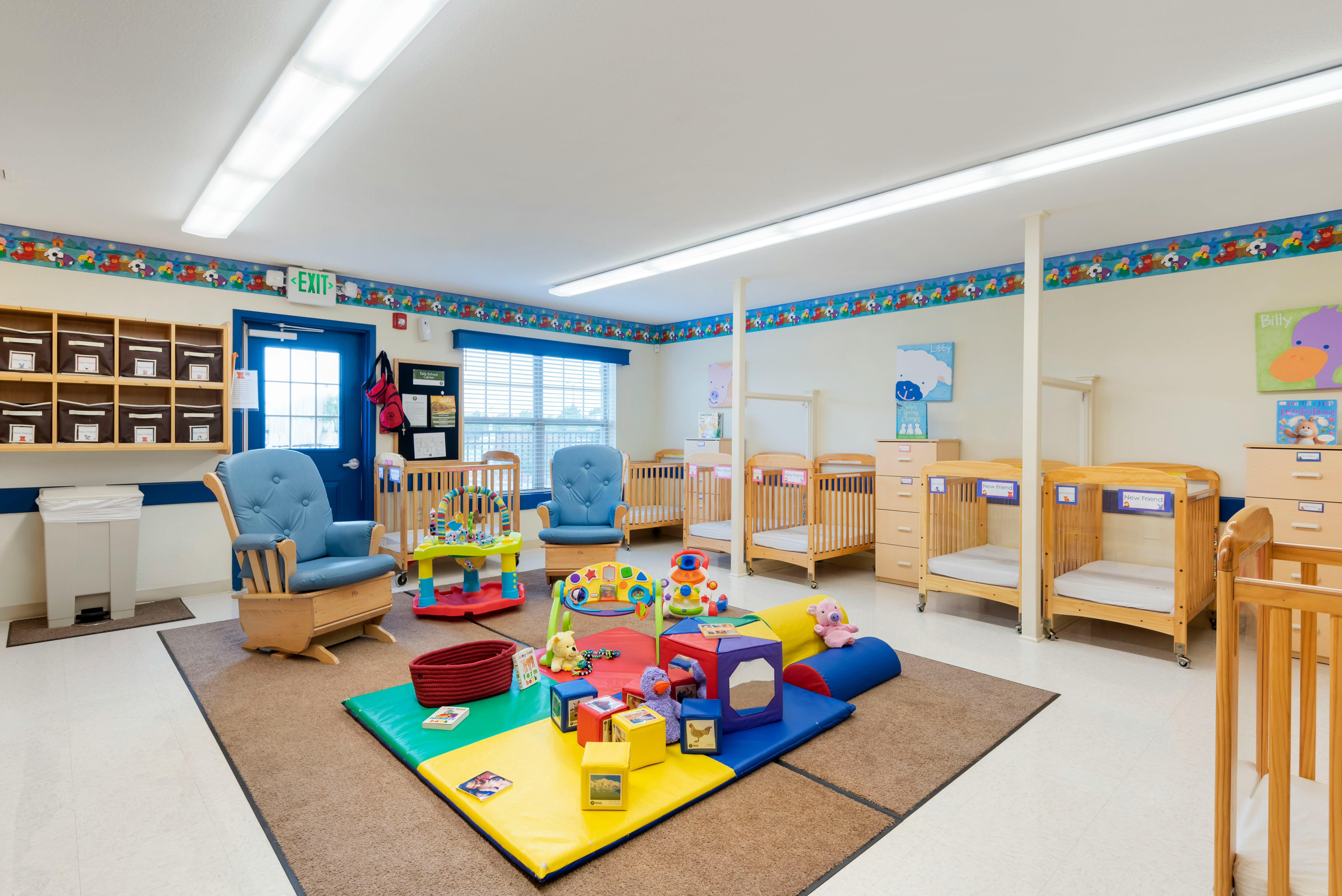 A childcare room with multiple cribs, two rocking chairs, and colorful play mats