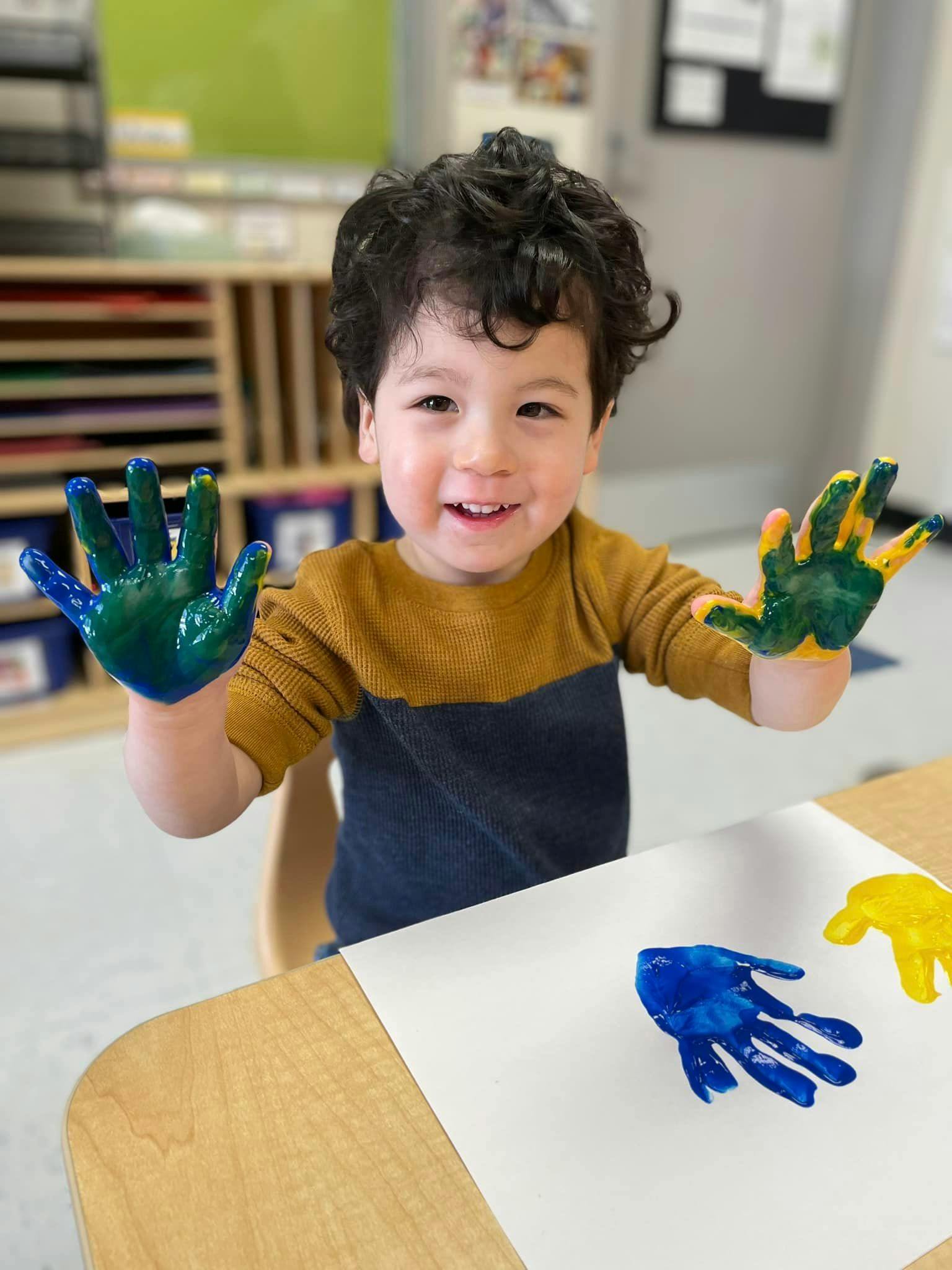 Child with paint on hands, making handprints on paper