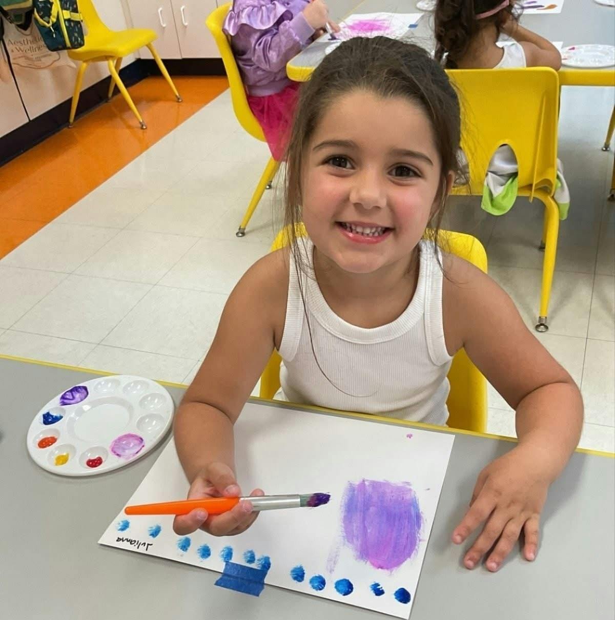 Child painting on paper at a table in a classroom