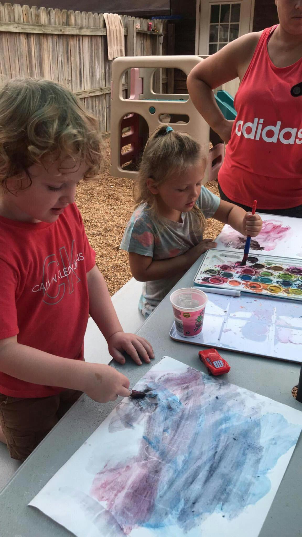 Two children painting at a table outdoors