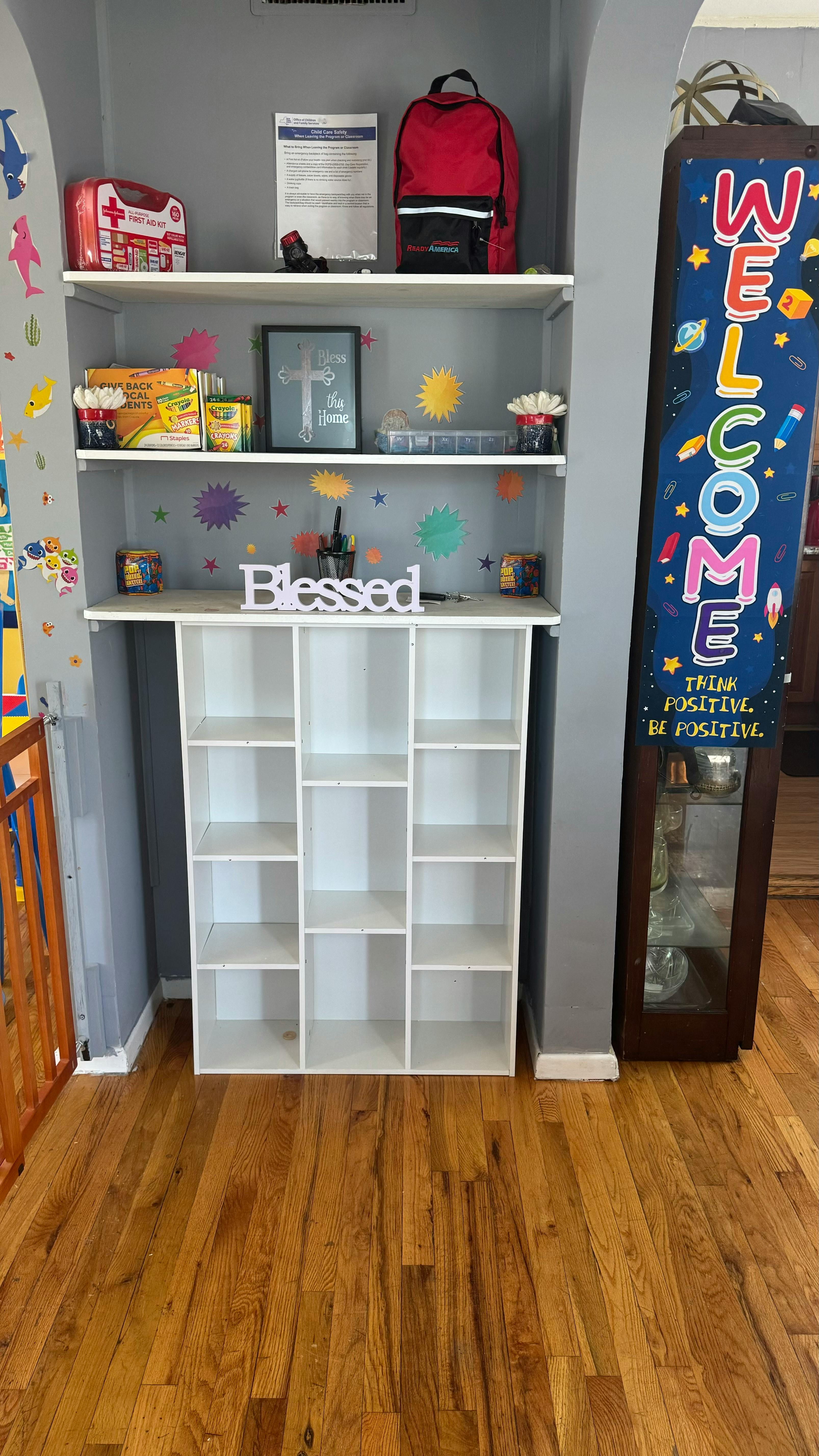 Shelves with a first aid kit, backpack, framed art, and a "Blessed" sign