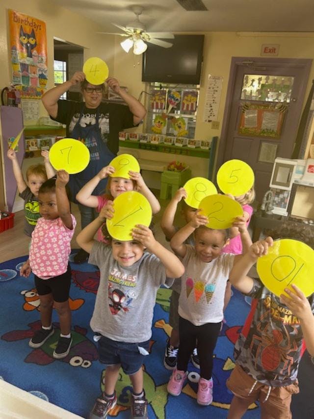 Adult and children holding yellow circles with numbers on their heads